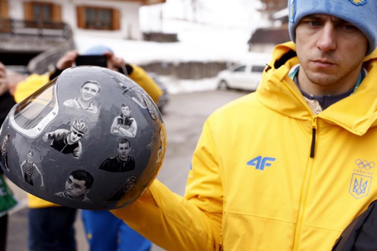 Ukraine's skeleton racer Vladyslav Heraskevych holds his helmet, which depicts victims of his country's war with Russia, in Cortina d'Ampezzo on February 12, 2026. Heraskevych was disqualified from the Winter Olympics on February 12, 2026 after refusing to back down over his banned helmet, which depicts victims of his country's war with Russia. The International Olympic Committee said he had been kicked out of the Milan-Cortina Games "after refusing to adhere to the IOC athlete expression guidelines". Odd ANDERSEN / AFP