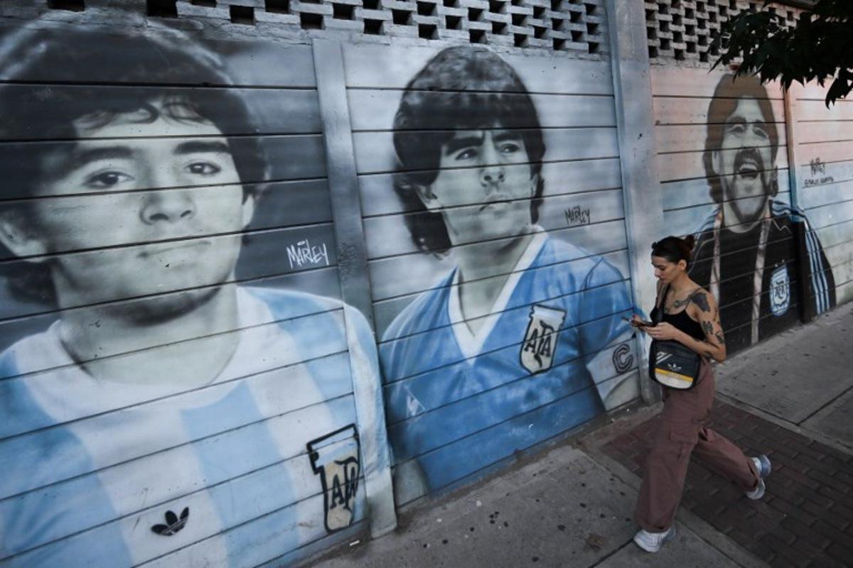 A woman walks past murals depicting late Argentine football legend Diego Maradona outside Diego Armando Maradona Stadium, home of the Argentine football team Argentinos Juniors at La Paternal neighborhood in Buenos Aires on March 10, 2025. At the "barrio de Dios," where Diego Maradona started playing professionally at the age of 15, every corner remembers the Argentine football deity. Four years after his death "in such strange conditions," those who live in this Buenos Aires neighborhood seek justice. LUIS ROBAYO / AFP