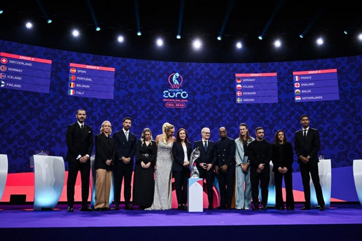 (From L) Italian former football player Leonardo Bonucci, Former Swiss football player Caroline Seger, German former football player Sami Khedira, TV host and Swiss sports presenter Annette Fetscherinas, UEFA head of women's football and German former football player Nadine Kessler, UEFA's Deputy General Secretary Giorgio Marchetti, TV host and former English football player Ian Wright, English former football player Jill Scott, Swiss football player Xherdan Shaqiri, Spanish football forward Veronica Boquete and French former football player Raphael Varane pose in front of a screen displaying fixtures of the group stage of the UEFA Women's Euro 2025 trophy after the draw in Lausanne, on December 16, 2024.  Fabrice COFFRINI / AFP