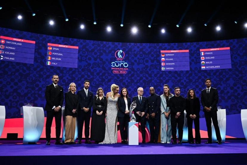 (From L) Italian former football player Leonardo Bonucci, Former Swiss football player Caroline Seger, German former football player Sami Khedira, TV host and Swiss sports presenter Annette Fetscherinas, UEFA head of women's football and German former football player Nadine Kessler, UEFA's Deputy General Secretary Giorgio Marchetti, TV host and former English football player Ian Wright, English former football player Jill Scott, Swiss football player Xherdan Shaqiri, Spanish football forward Veronica Boquete and French former football player Raphael Varane pose in front of a screen displaying fixtures of the group stage of the UEFA Women's Euro 2025 trophy after the draw in Lausanne, on December 16, 2024.  Fabrice COFFRINI / AFP
