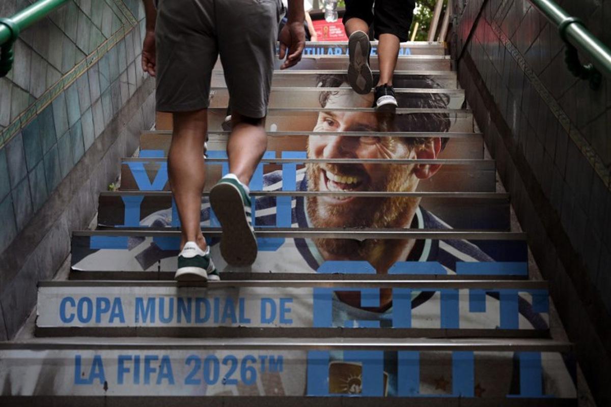 People leave a subway station with an advertising of Argentina´s National football team jersey and the portrait of Argentina's forward Lionel Messi in Buenos Aires on February 24, 2026.  JUAN MABROMATA / AFP