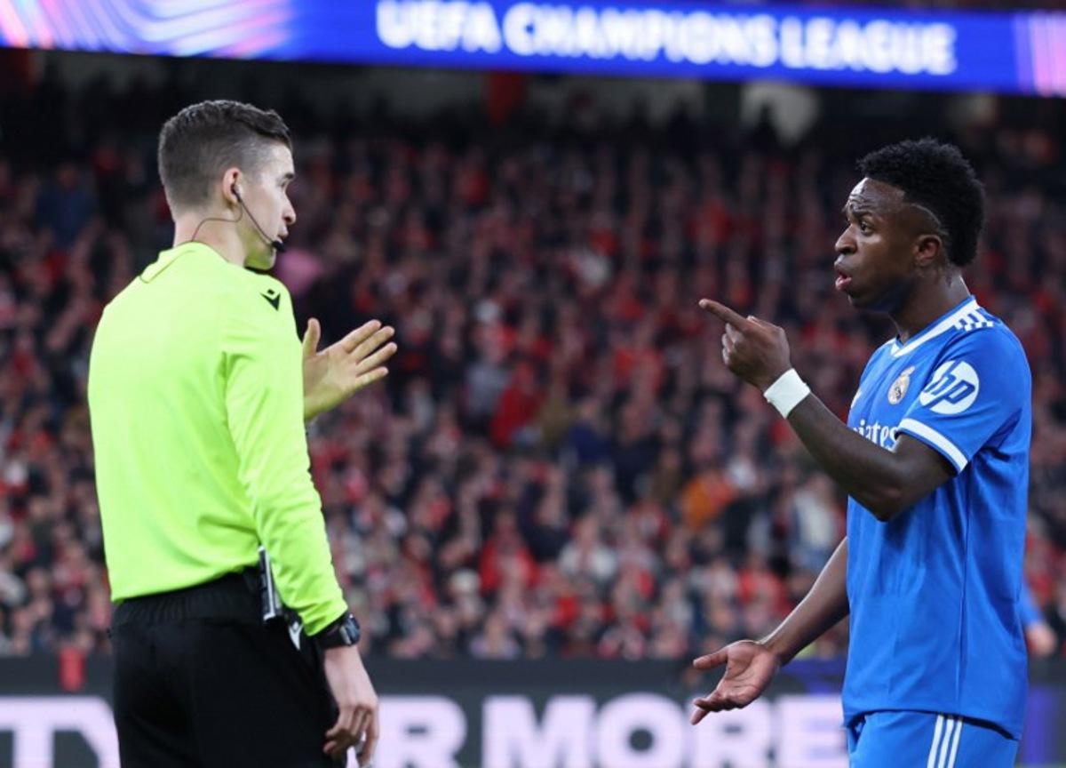 Real Madrid's Brazilian forward #07 Vinicius Junior talks with French referee Francois Letexier during the UEFA Champions League knockout round play-off first leg football match between SL Benfica and Real Madrid CF at Estadio da Luz in Lisbon on February 17, 2026.  PATRICIA DE MELO MOREIRA / AFP