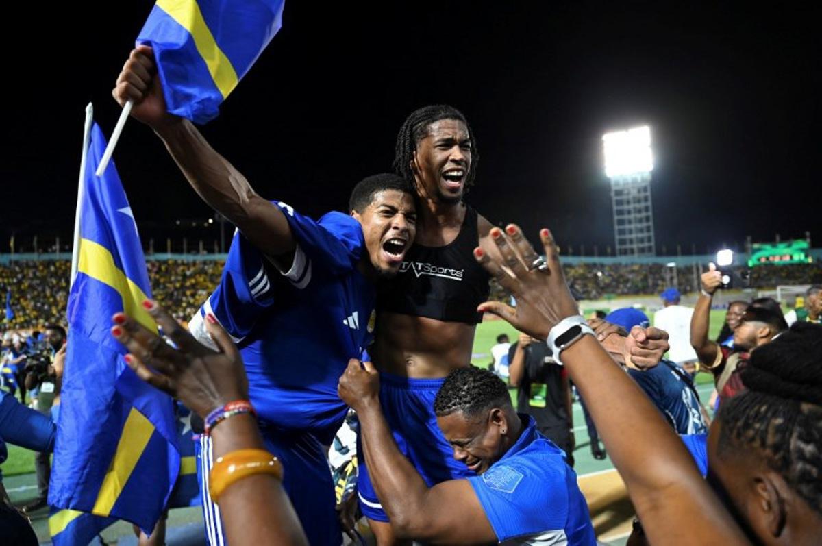 Curaçao players and fans celebrate World Cup 2026 qualification after a 0-0 draw with Jamaica at the National Stadium in Kingston, Jamaica on November 18, 2025. The tiny Caribbean nation of Curacao became the smallest country ever to qualify for the World Cup on November 18 as Haiti booked their return to the tournament for the first time in 52 years along with Panama. A nerve-shredding finale to the CONCACAF qualifying campaign saw Curacao -- with a population of just 156,000 -- squeeze into next year's finals in the United States, Canada and Mexico with a 0-0 draw against Jamaica in Kingston.  Ricardo MAKYN / AFP