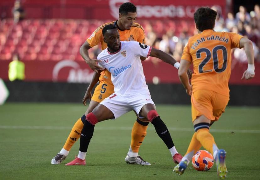 Sevilla's Belgian forward #11 Dodi Lukebakio (C) fights for the ball with Real Madrid's English midfielder #05 Jude Bellingham during the Spanish league football match between Sevilla FC and Real Madrid CF at Ramon Sanchez Pizjuan Stadium in Seville on May 18, 2025.  CRISTINA QUICLER / AFP