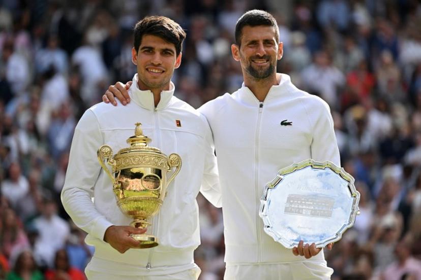 Spain's Carlos Alcaraz holding the winner's trophy (L) and second-placed Serbia's Novak Djokovic pose for pictures during the price ceremony at the end of their men's singles final tennis match on the fourteenth day of the 2024 Wimbledon Championships at The All England Lawn Tennis and Croquet Club in Wimbledon, southwest London, on July 14, 2024. Defending champion Alcaraz beat seven-time winner Novak Djokovic in a blockbuster final, with Alcaraz winning 6-2, 6-2, 7-6. ANDREJ ISAKOVIC / AFP