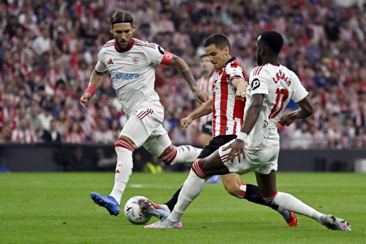 Sevilla's Serbian midfielder #06 Nemanja Gudelj (L), Athletic Bilbao's Spanish midfielder #16 Inigo Ruiz de Galarreta and Sevilla's Belgian forward #10 Dodi Lukebakio fight for the ball during the Spanish league football match between Athletic Club Bilbao and Sevilla FC at San Mames Stadium in Bilbao on August 17, 2025.  ANDER GILLENEA / AFP