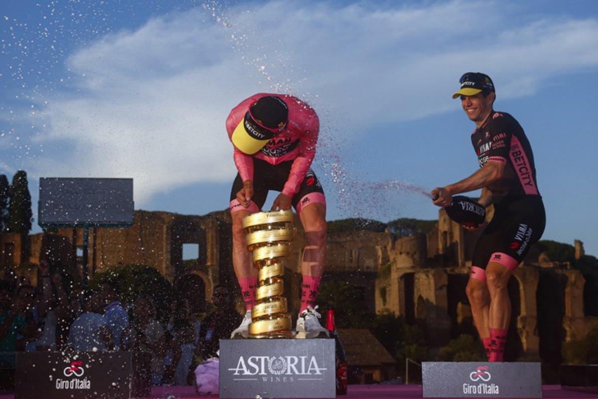 Team Visma-Lease a Bike's British rider Simon Yates (L) wearing the pink jersey of overall leader (Maglia Rosa) celebrates holding the Trofeo Senza Fine on the podium with teammate Team Visma-Lease a Bike's Belgian rider Wout Van Aert after the 21st and last stage and winning the 108th Giro d'Italia cycling race of 143kms from Rome to Rome on June 1, 2025.  Luca Bettini / AFP