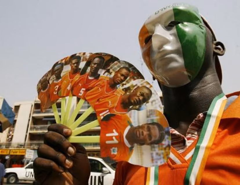 A supporter of the Elephants, the Ivorian national football team, wearing a mask with the Ivorian colours, waves a fan with portraits of the players 24 January 2008 in Abidjan. Ghana's Michael Essien is relishing the prospect of coming up against his Chelsea teammate Didier Drogba's Ivory Coast in the African Nations Cup final. AFP PHOTO / KAMBOU SIA