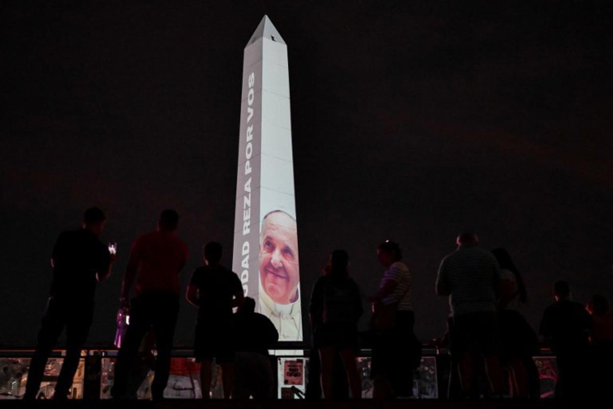 People look at the obelisk illuminated with the image of Pope Francis in Buenos Aires on February 24, 2025. Pope Francis, hospitalized due to bilateral pneumonia, remains in critical condition but is showing "slight improvement," the Vatican announced Monday night, as concern grows for the 88-year-old Argentine pontiff. LUIS ROBAYO / AFP